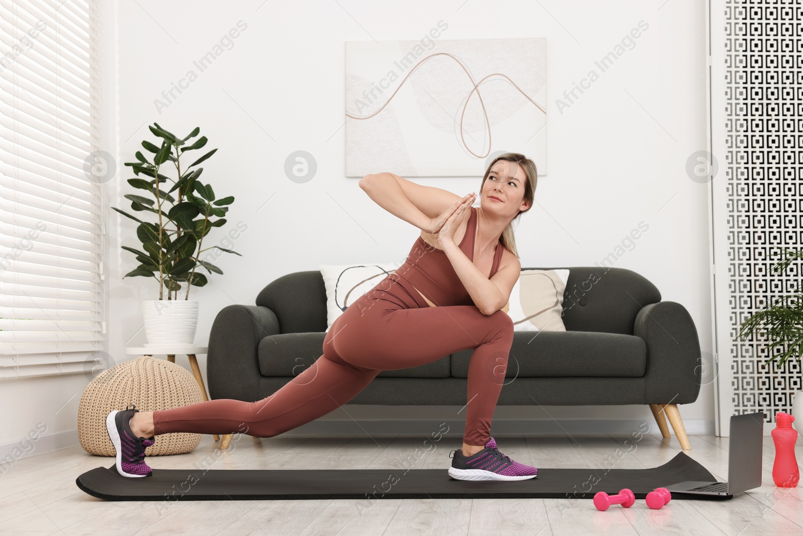 Photo of Online fitness trainer. Woman doing exercise near laptop at home