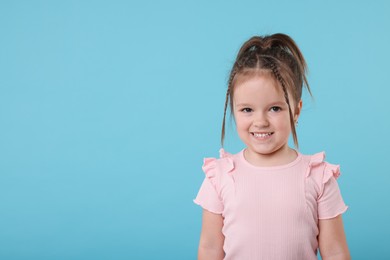 Portrait of cute little girl on light blue background, space for text