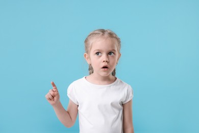 Photo of Cute little girl pointing at something on light blue background, space for text