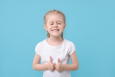 Photo of Cute little girl showing thumbs up on light blue background