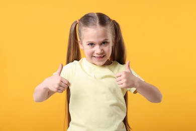 Photo of Cute little girl showing thumbs up on orange background
