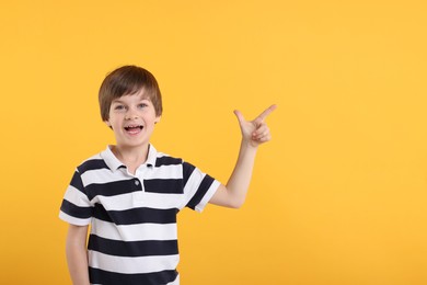 Cute little boy pointing at something on orange background, space for text