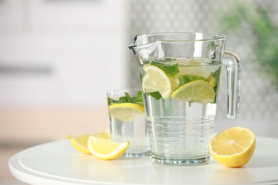 Photo of Refreshing lemonade with mint in jug and glass on white table. Space for text