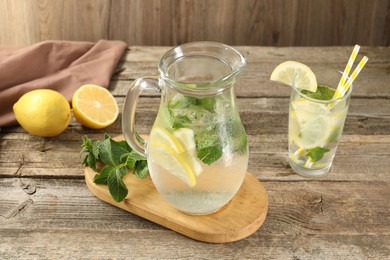 Refreshing lemonade with mint in jug and glass on wooden table