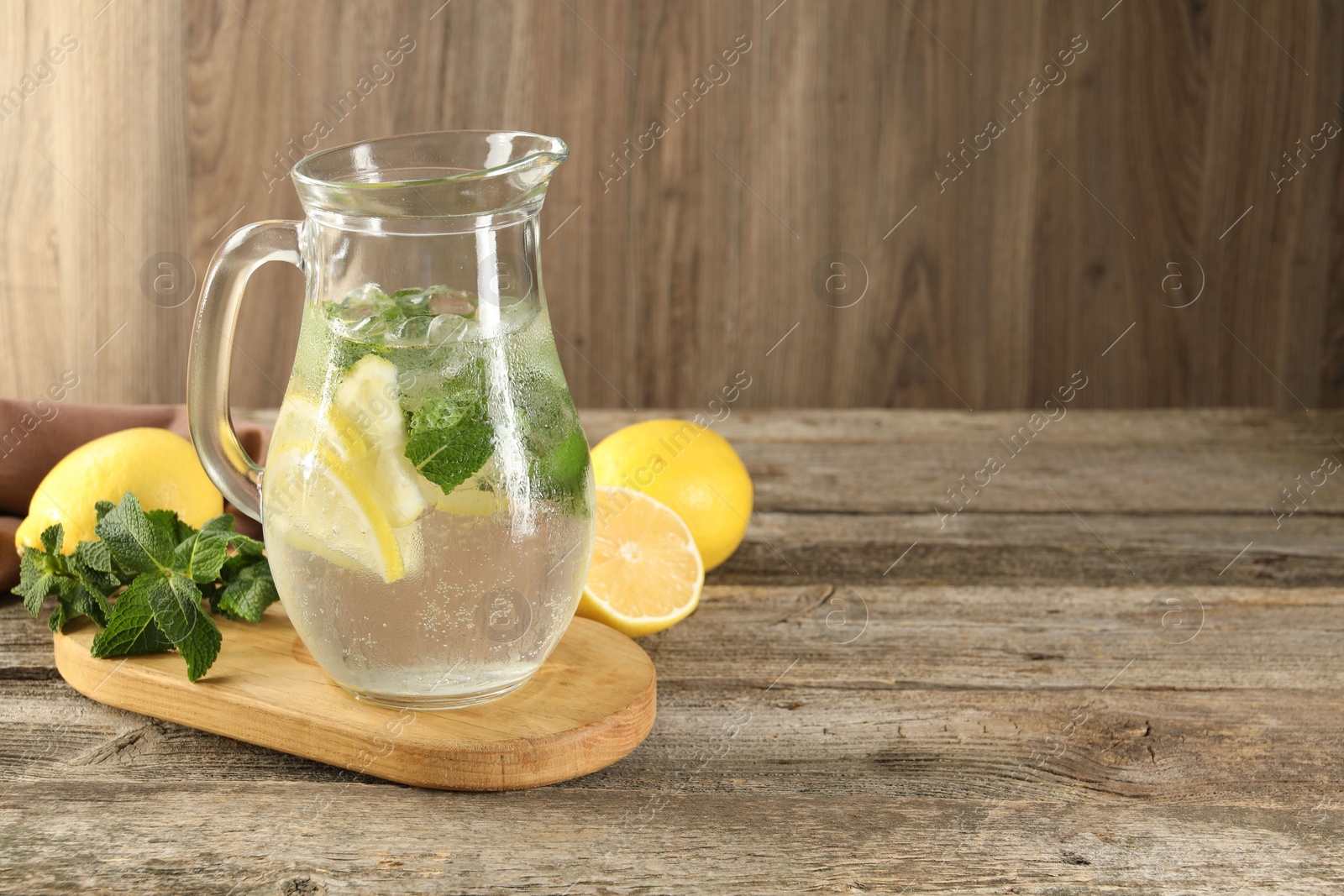 Photo of Refreshing lemonade with mint in jug and ingredients on wooden table, space for text