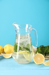 Refreshing lemonade with mint in jug and ingredients on light blue wooden table