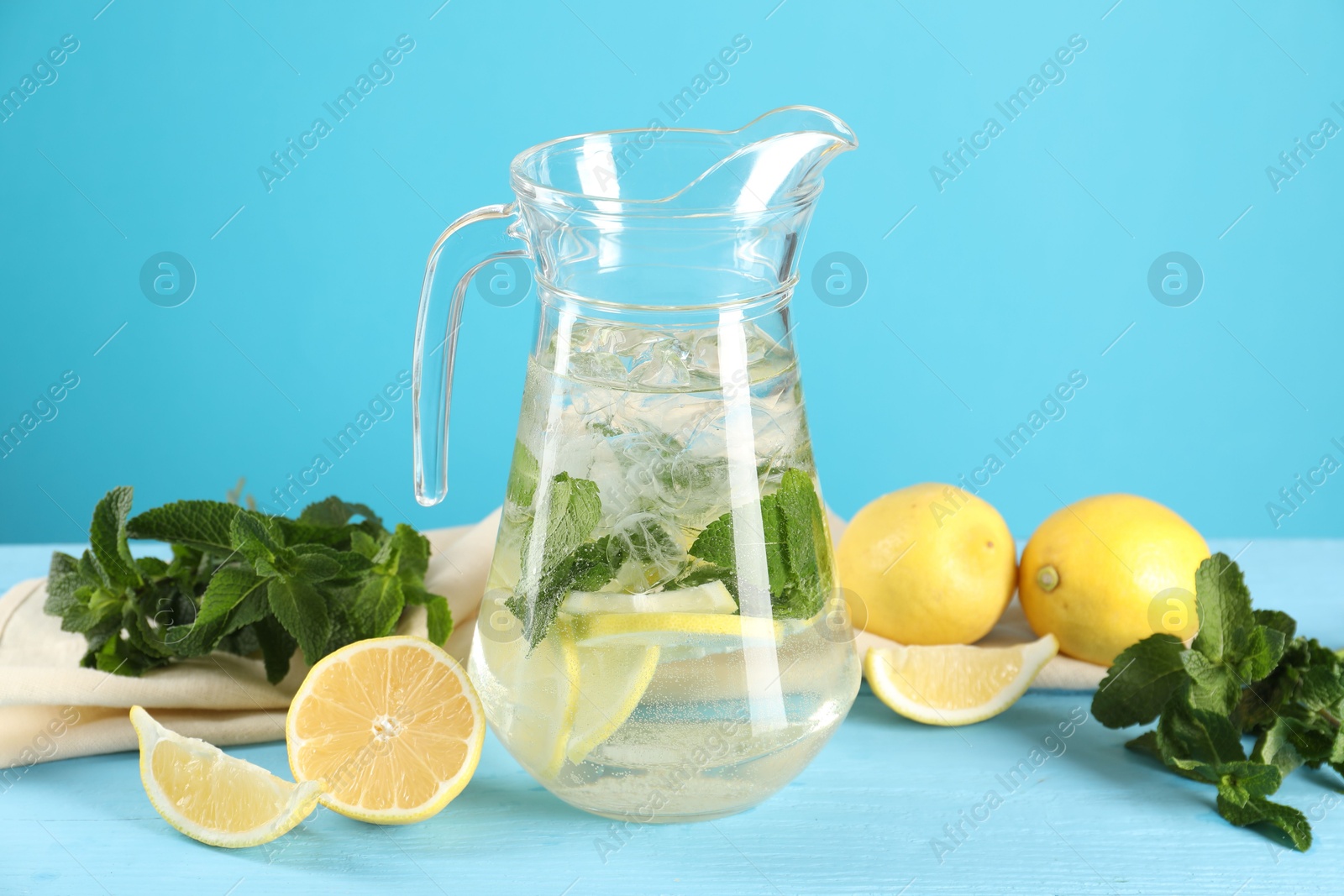 Photo of Refreshing lemonade with mint in jug and ingredients on light blue wooden table