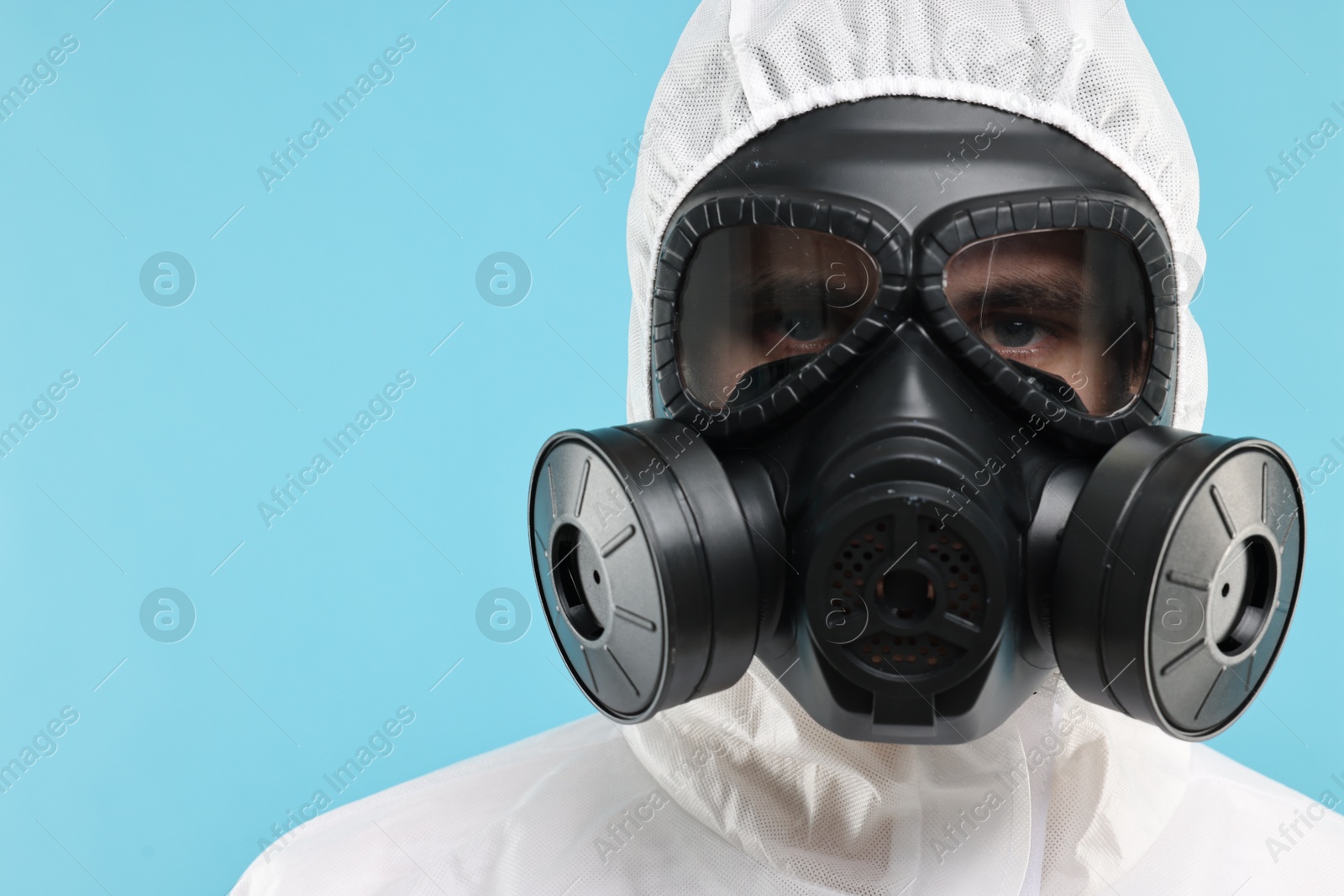 Photo of Worker in gas mask on light blue background, closeup. Space for text