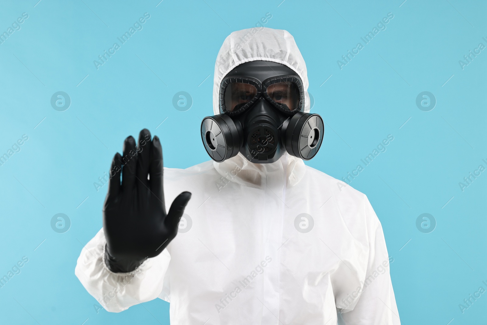 Photo of Worker in gas mask showing stop gesture on light blue background