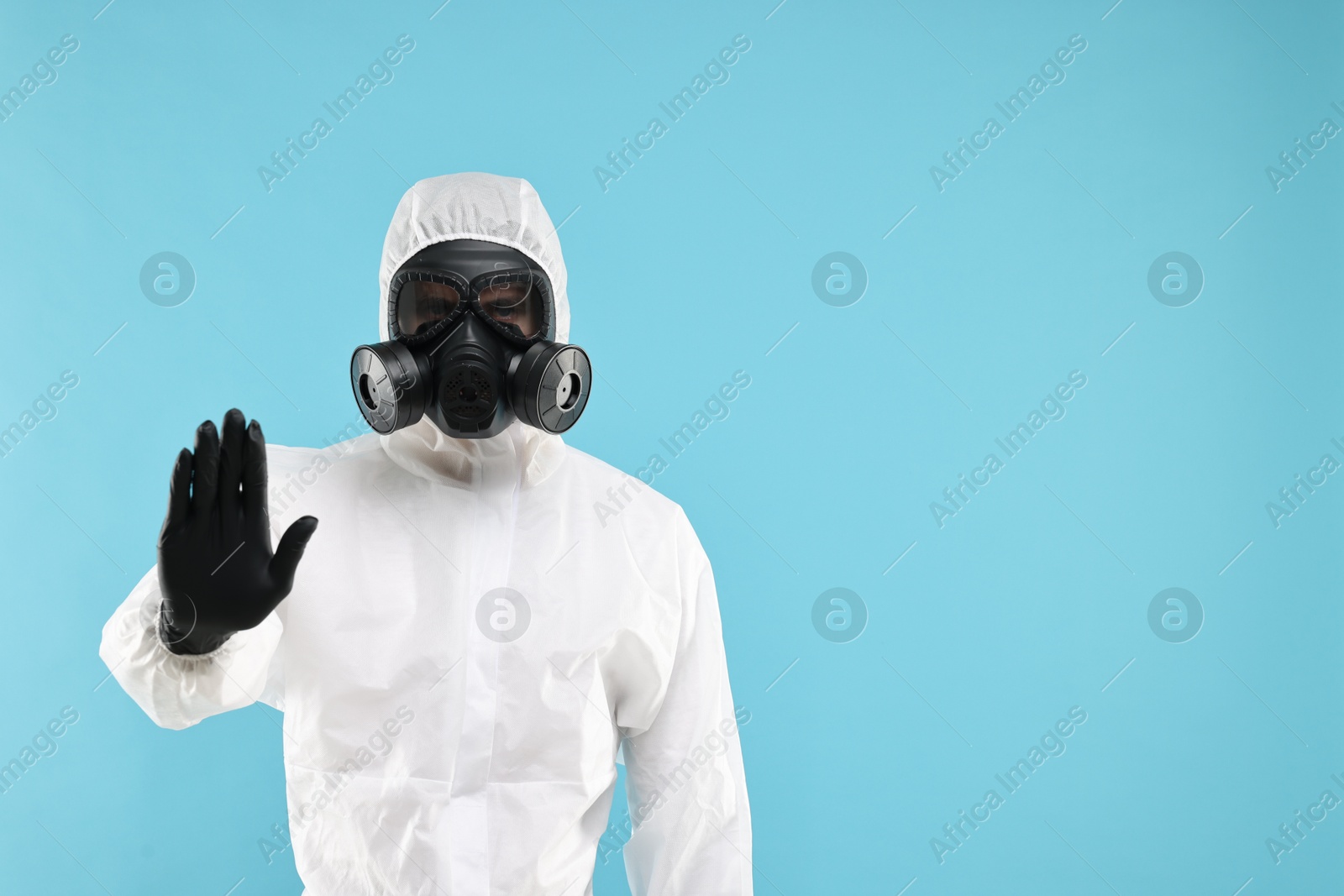 Photo of Worker in gas mask showing stop gesture on light blue background. Space for text