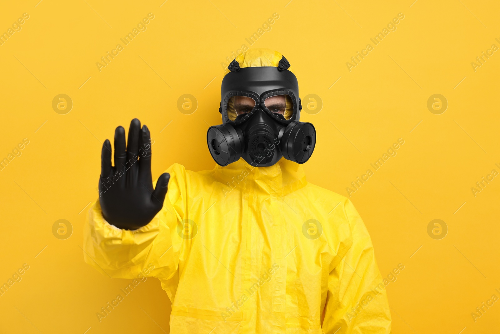 Photo of Worker in gas mask showing stop gesture on yellow background