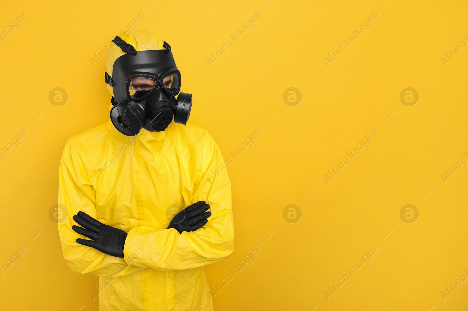 Photo of Worker in gas mask with crossed arms on yellow background. Space for text