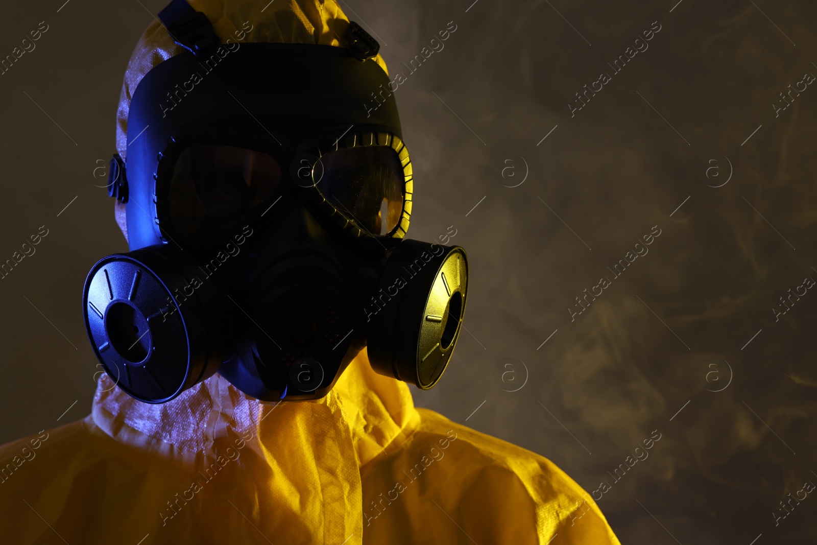 Photo of Worker wearing gas mask in smoke on dark background, closeup. Space for text