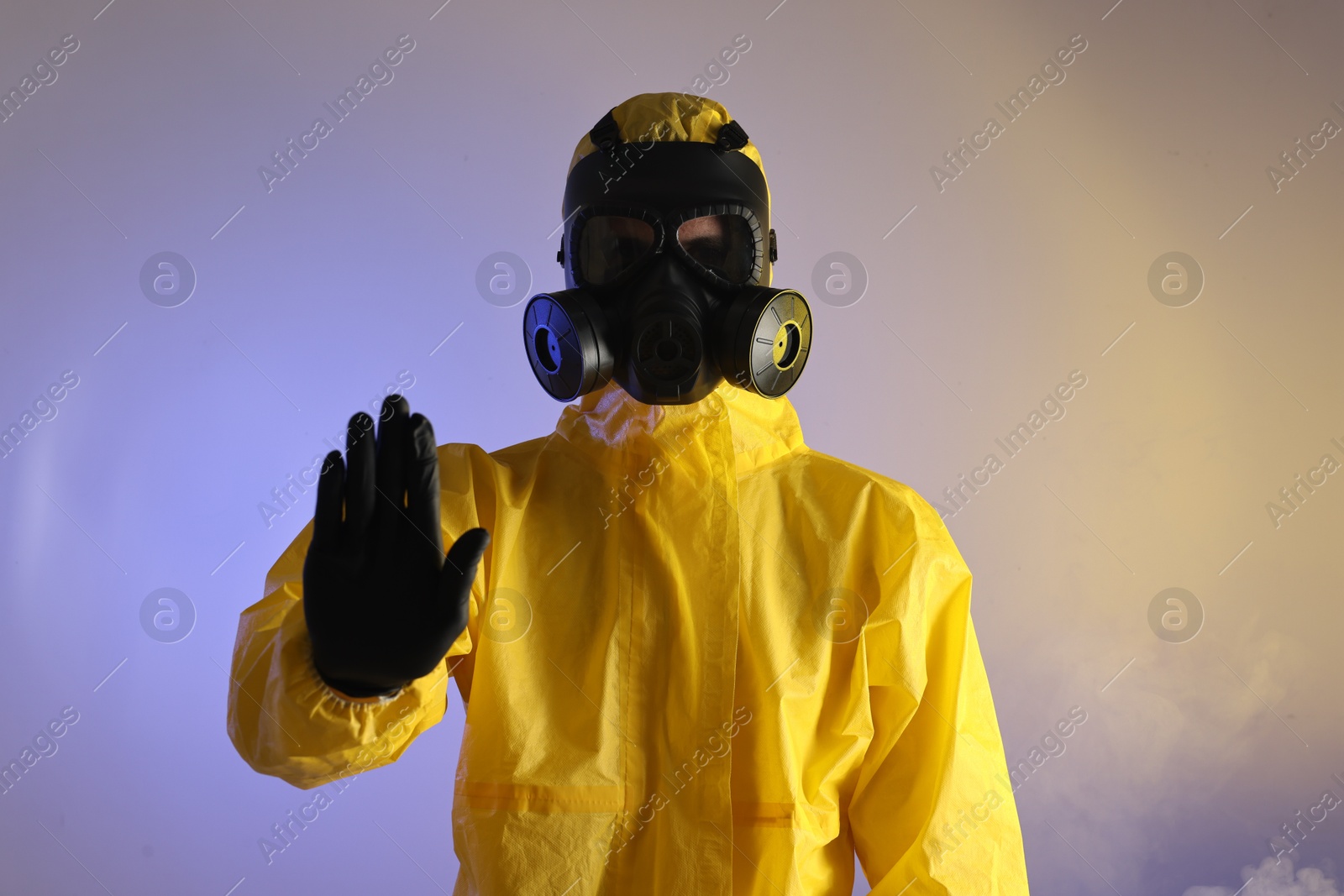 Photo of Worker wearing gas mask in smoke showing stop gesture on violet background