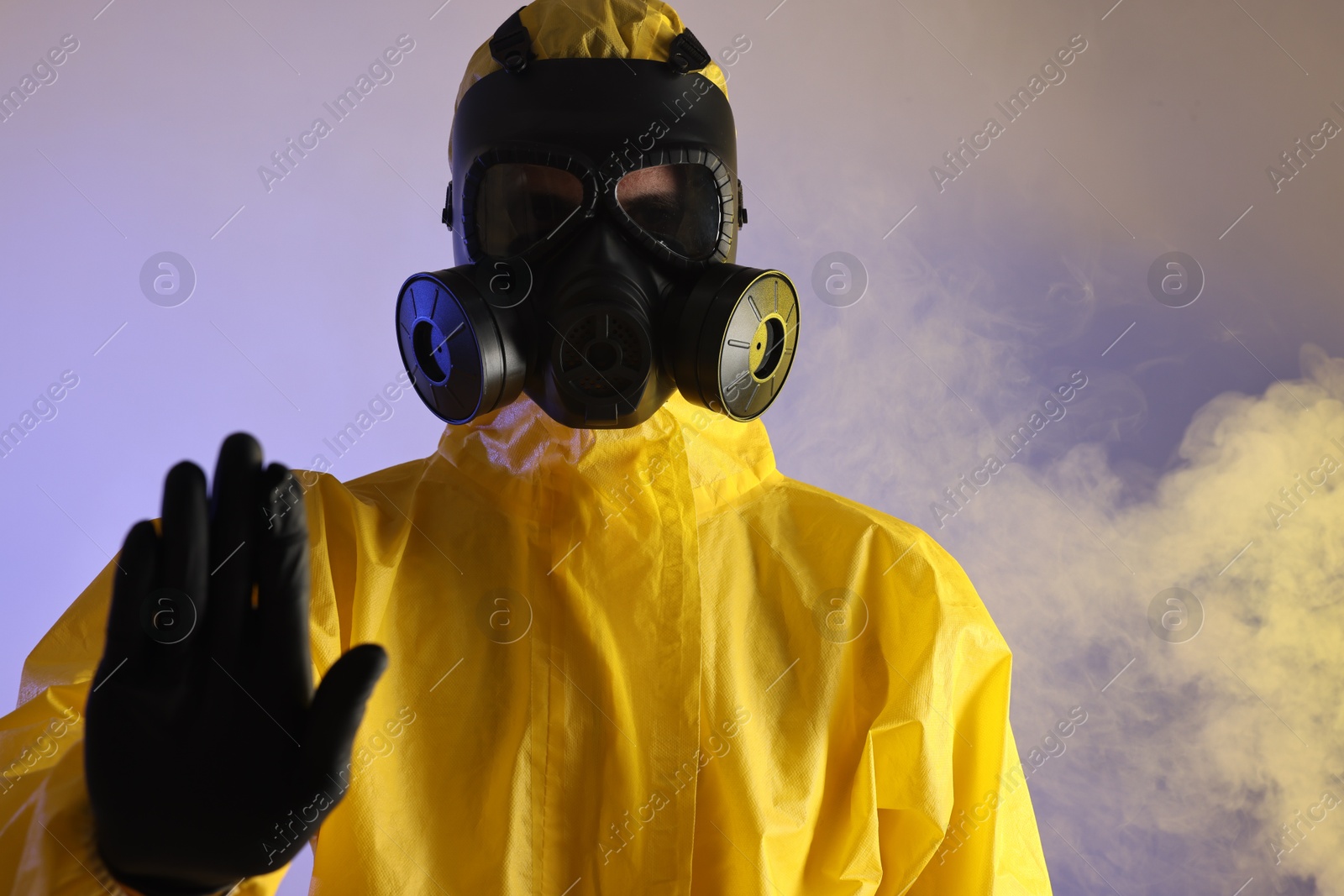 Photo of Worker wearing gas mask in smoke showing stop gesture on violet background