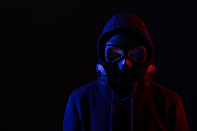 Photo of Man wearing gas mask in color lights on black background. Space for text