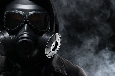 Photo of Man wearing gas mask in smoke on black background, closeup. Space for text