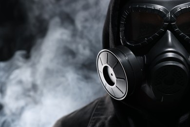 Photo of Man wearing gas mask in smoke on black background, closeup. Space for text