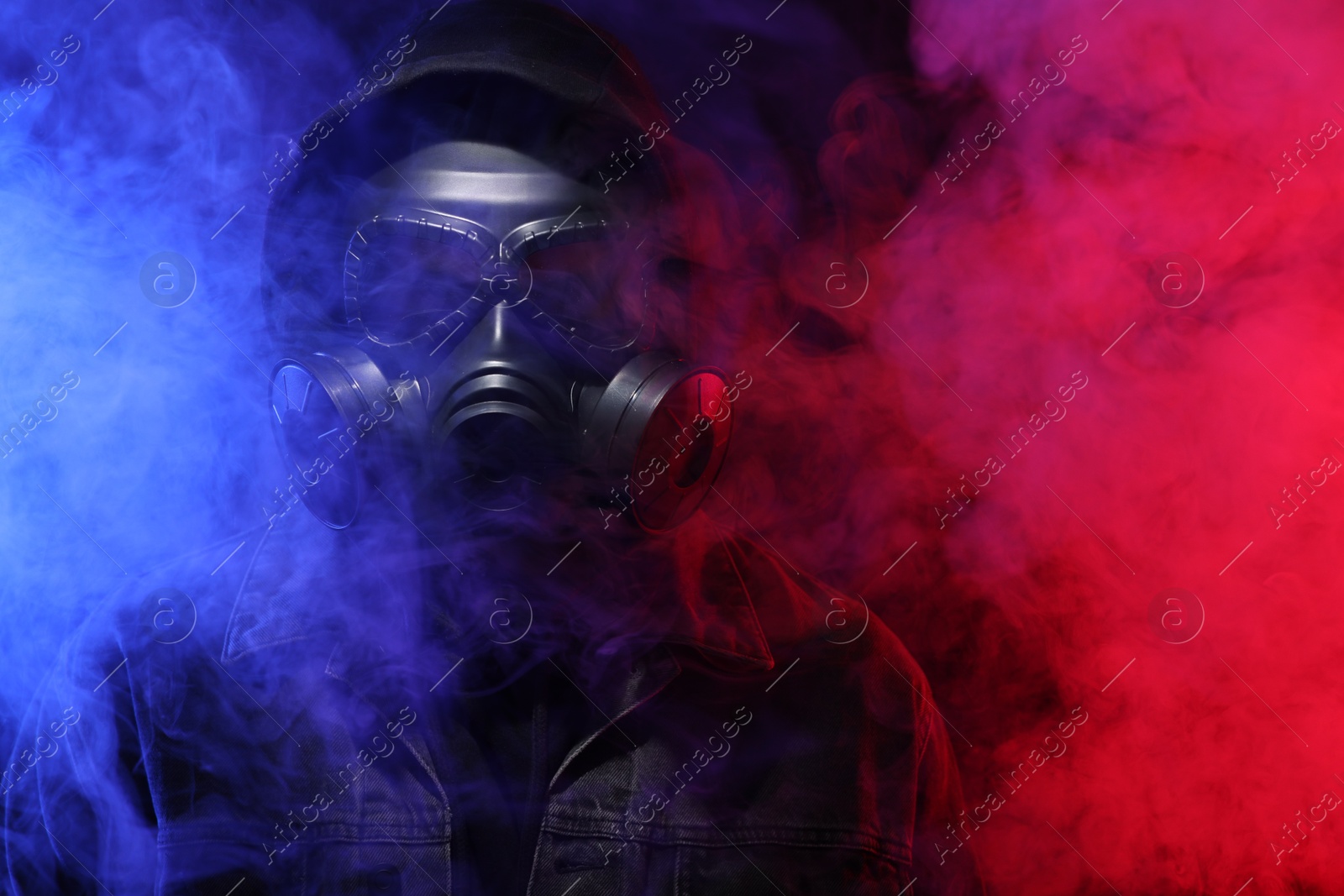 Photo of Man wearing gas mask in color lights and smoke on black background. Space for text