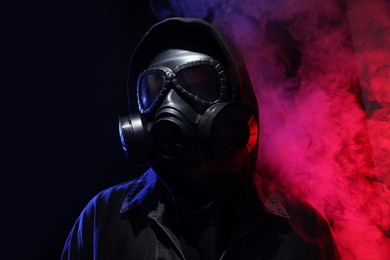 Photo of Man wearing gas mask in color lights and smoke on black background