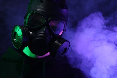 Man wearing gas mask in color lights on black background, closeup. Space for text