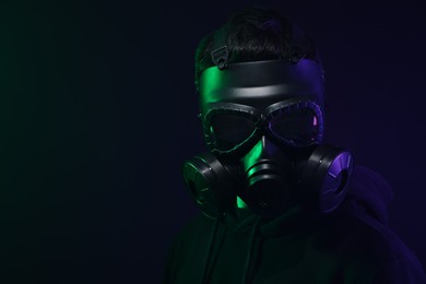 Man wearing gas mask in color lights on black background. Space for text