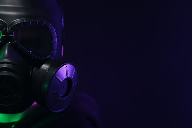 Photo of Man wearing gas mask in color lights on black background, closeup. Space for text