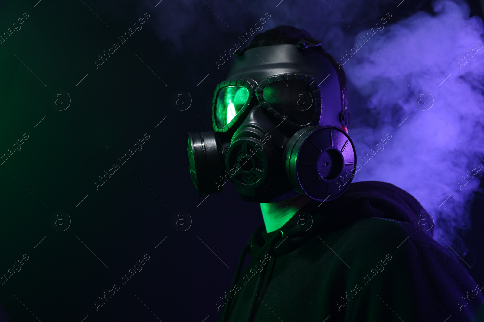 Photo of Man wearing gas mask in color lights and smoke on black background. Space for text