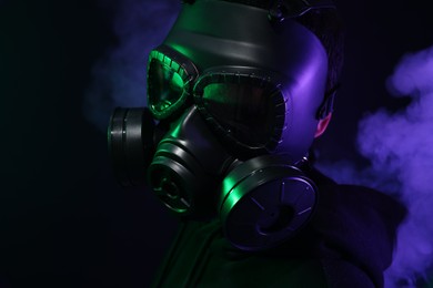 Man wearing gas mask in color lights and smoke on black background
