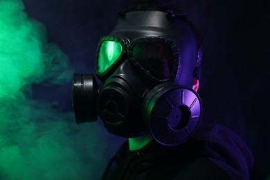 Man wearing gas mask in color lights and smoke on black background