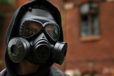 Man in gas mask near building outdoors. Space for text