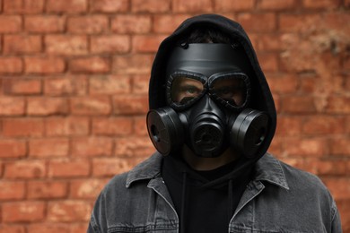 Man in gas mask near red brick wall outdoors. Space for text