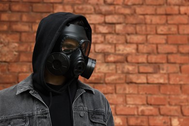 Photo of Man in gas mask near red brick wall outdoors. Space for text