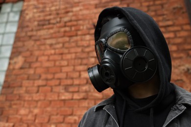 Photo of Man in gas mask near red brick wall outdoors, low angle view. Space for text