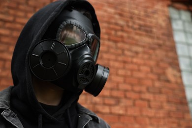 Photo of Man in gas mask near red brick wall outdoors, low angle view. Space for text