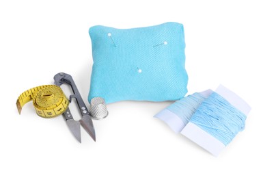 Photo of Light blue pincushion with sewing pins, cutter, threads, thimble and measuring tape isolated on white