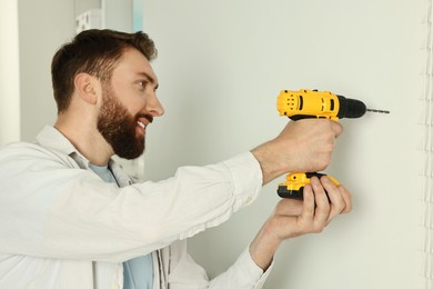 Photo of Smiling man drilling white wall at home