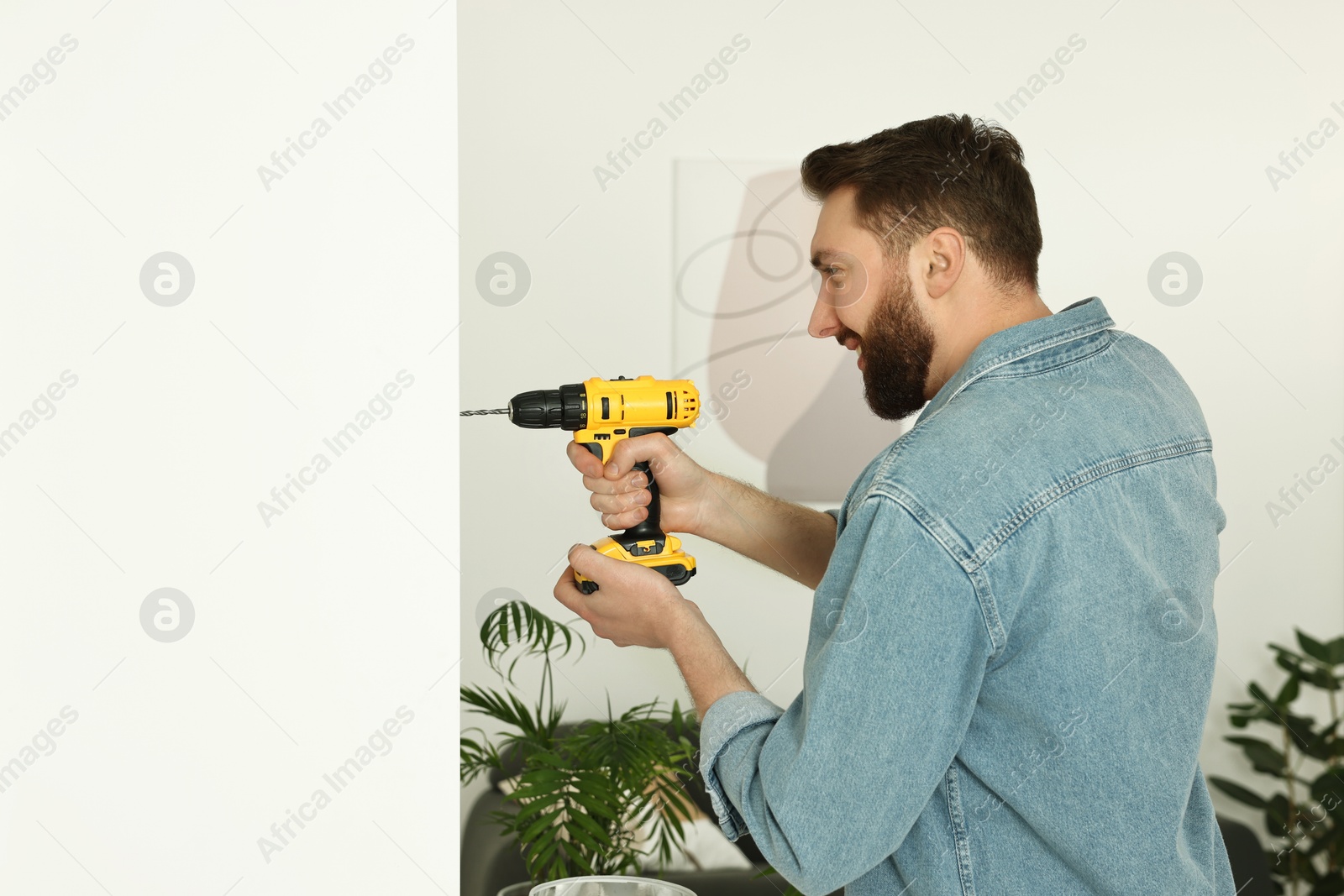 Photo of Smiling man working with drill and wall at home