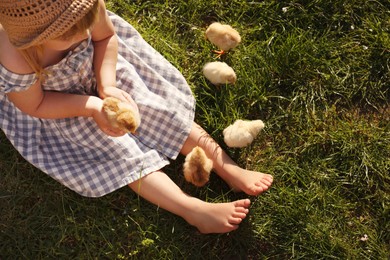 Photo of Little girl with cute chicks on green grass outdoors, top view
