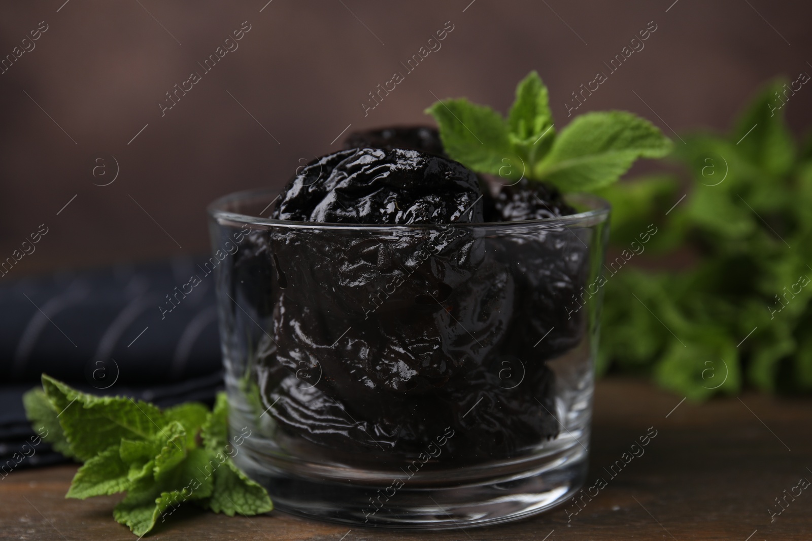 Photo of Tasty dried plums (prunes) in glass bowl and mint leaves on wooden table, closeup