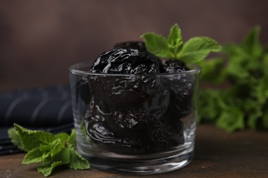 Tasty dried plums (prunes) in glass bowl and mint leaves on wooden table, closeup