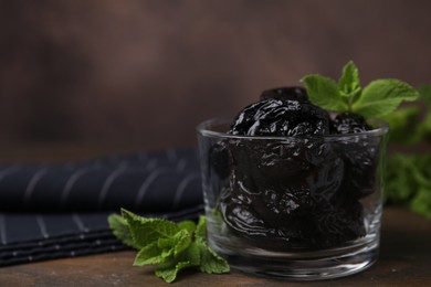 Tasty dried plums (prunes) in glass bowl and mint leaves on wooden table, closeup. Space for text