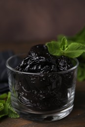 Tasty dried plums (prunes) in glass bowl and mint leaves on wooden table, closeup