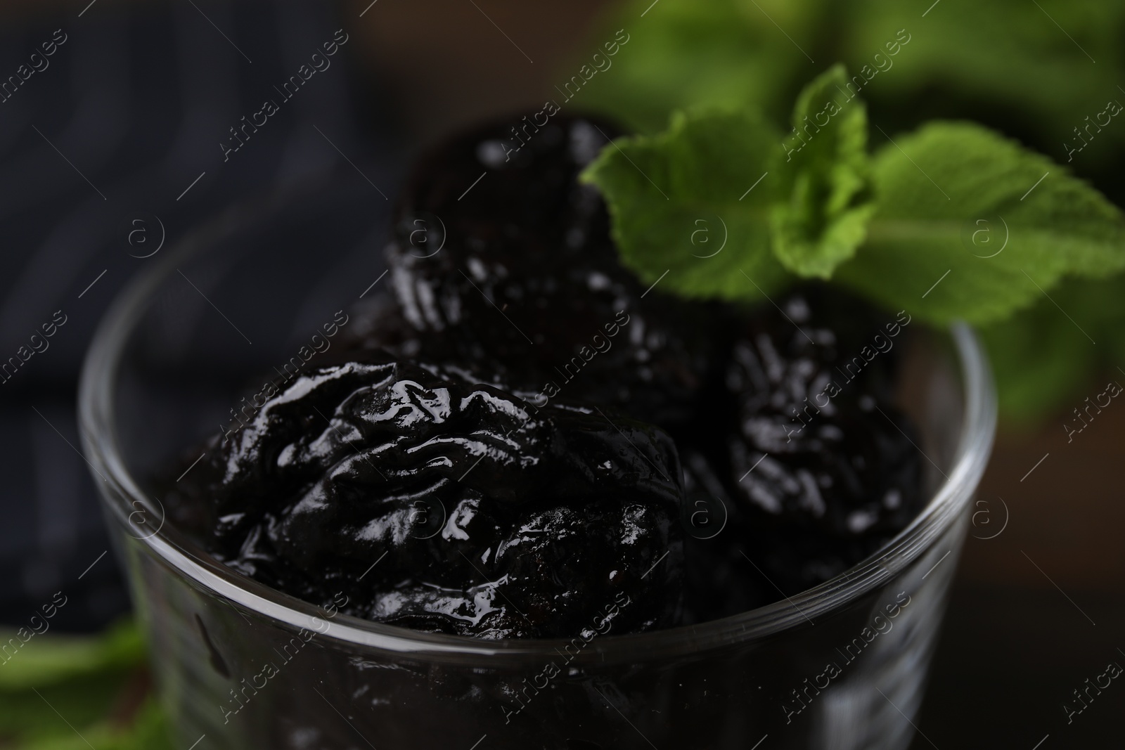 Photo of Tasty dried plums (prunes) and mint leaves in glass bowl, closeup