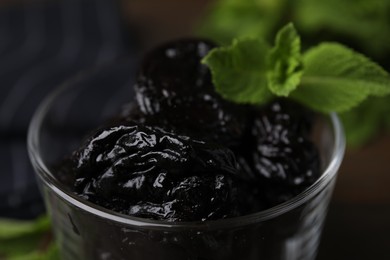 Tasty dried plums (prunes) and mint leaves in glass bowl, closeup