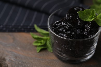 Tasty dried plums (prunes) in glass bowl and mint leaves on wooden table, closeup. Space for text