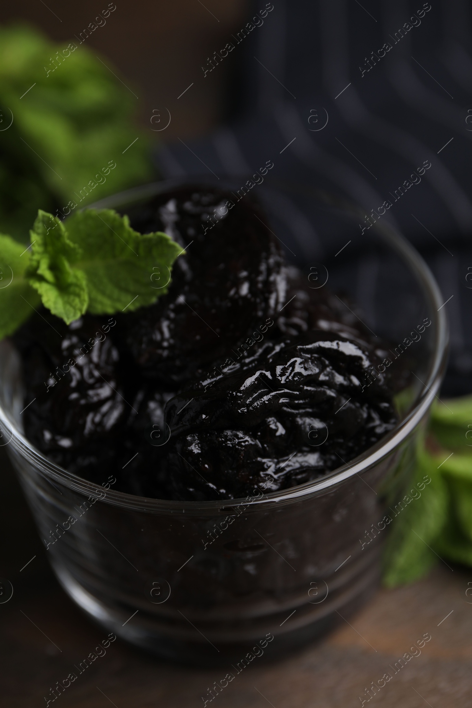 Photo of Tasty dried plums (prunes) in glass bowl and mint leaves on wooden table, closeup