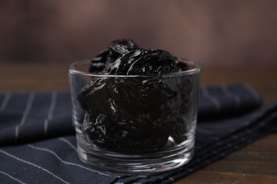 Tasty dried plums (prunes) in glass bowl on wooden table, closeup