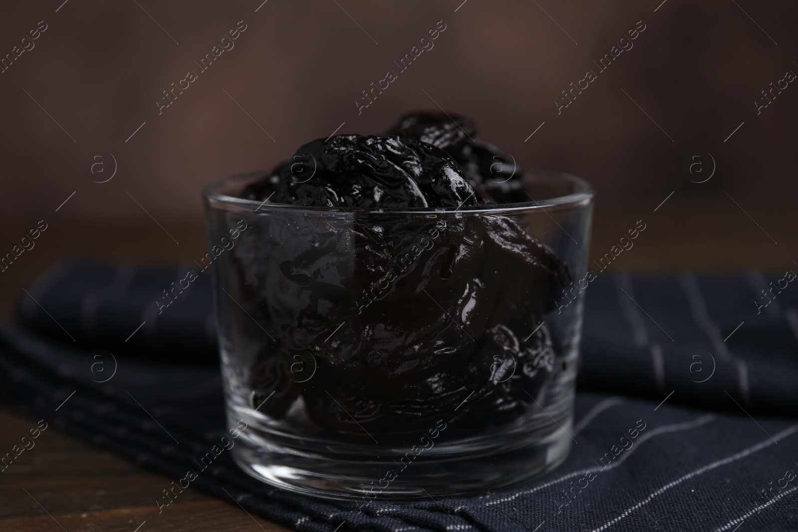 Photo of Tasty dried plums (prunes) in glass bowl on wooden table, closeup