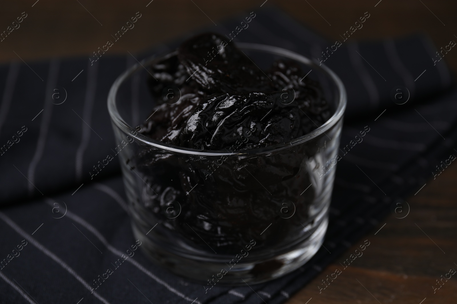 Photo of Tasty dried plums (prunes) in glass bowl on wooden table, closeup